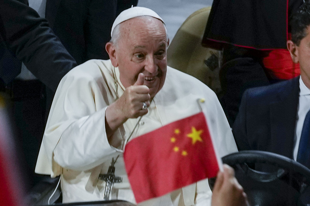 Francis smiles and gives thumbs up, foregrounded is small, hand-held Chinese flag.