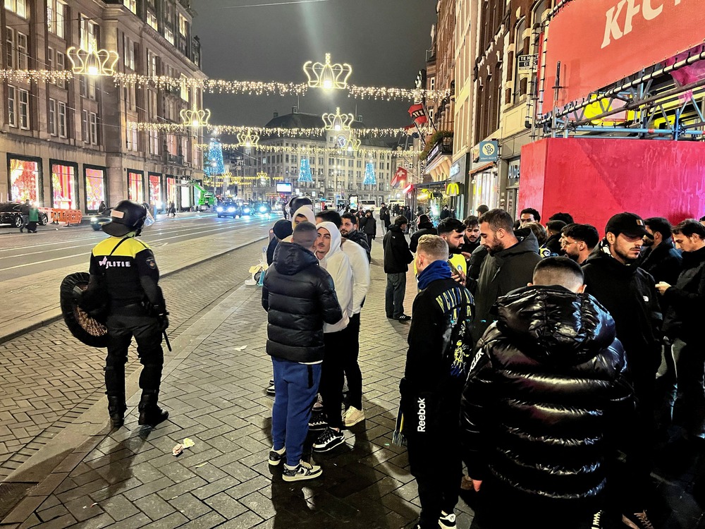 People stand on street wearing coats, assembled are police.