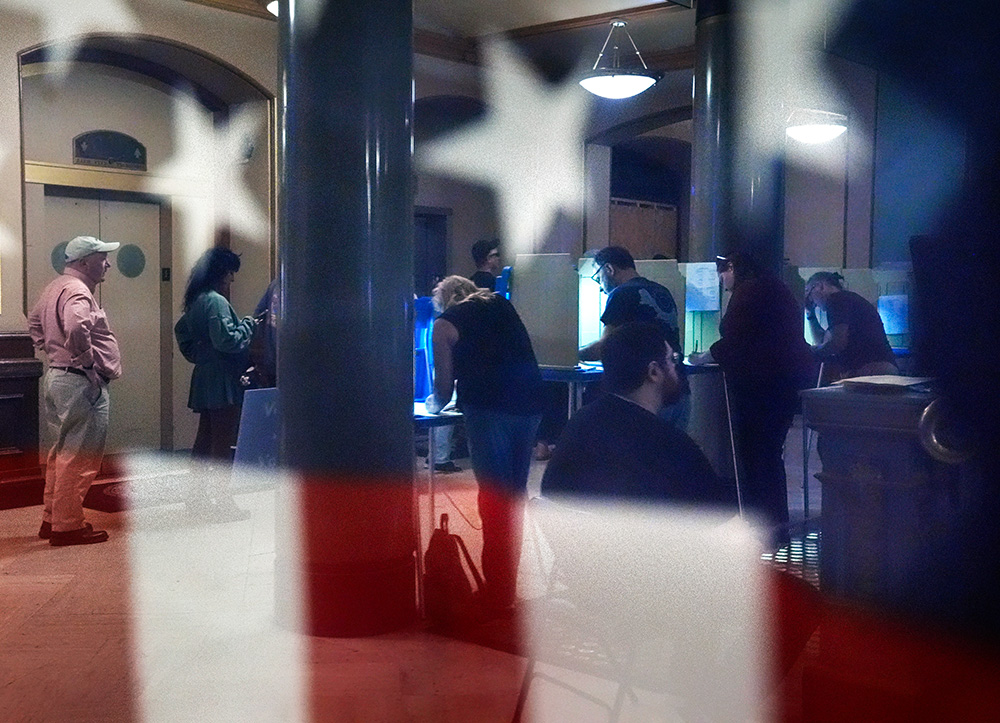 Voters are reflected in a window near an American flag as they mark their ballots during early voting in the general election on Nov. 1, 2024, at City Hall in Providence, R.I. (AP/Steven Senne)