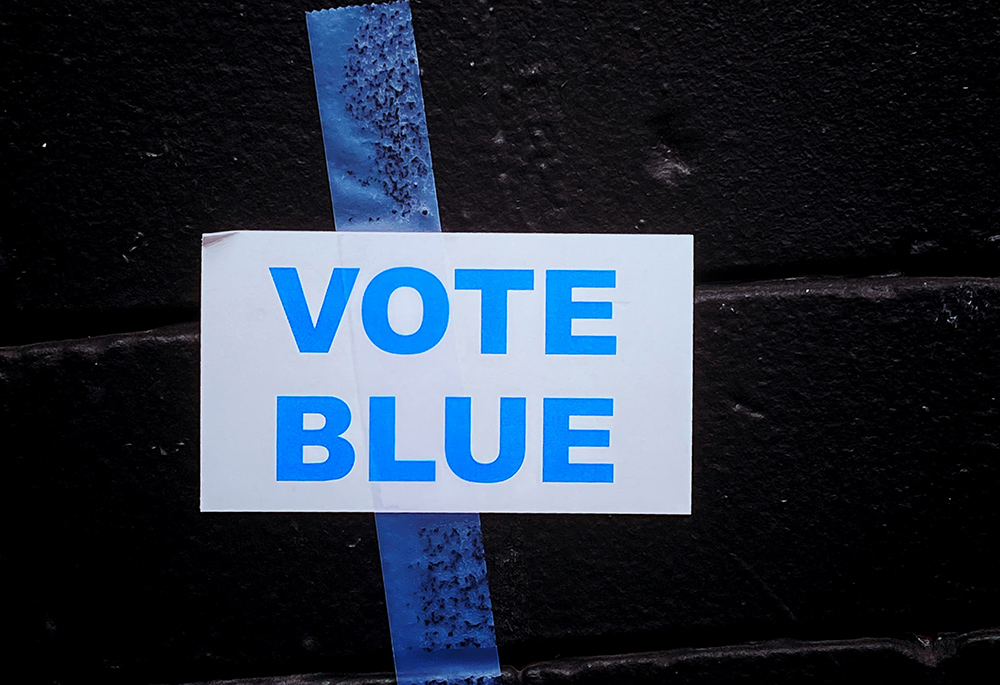 A sign reading "Vote blue" is taped against a black wall. (Unsplash/Jon Tyson)