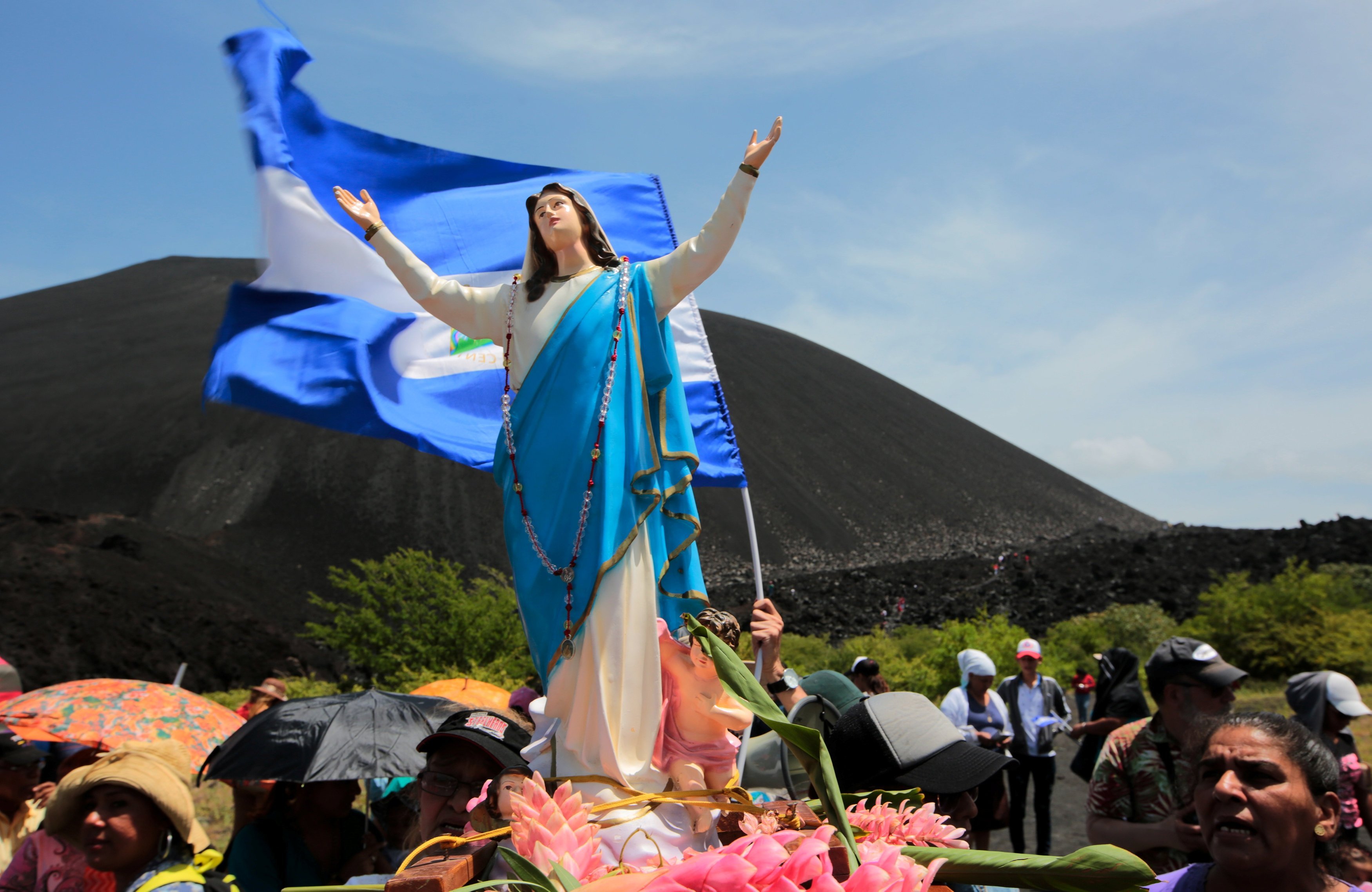 Statue of Mary as the Immaculate Conception carried by people, behind her waves Nicaraguan flag.