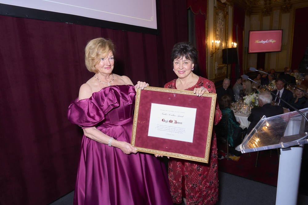 Benson wears gown and receives large framed certificate from another woman wearing gown. 