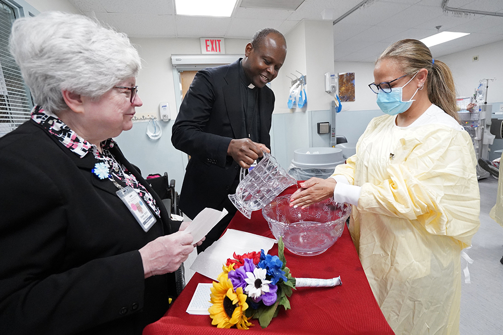 Fr. Francois X. Eale, chaplain at St. Catherine of Siena Hospital in Smithtown, N.Y., uses water as he blesses the hands of nurse Merissa Williams May 10, 2023. Looking on is Ursuline Sr. Edith Menegus, pastoral care director. (OSV News/Gregory A. Shemitz)