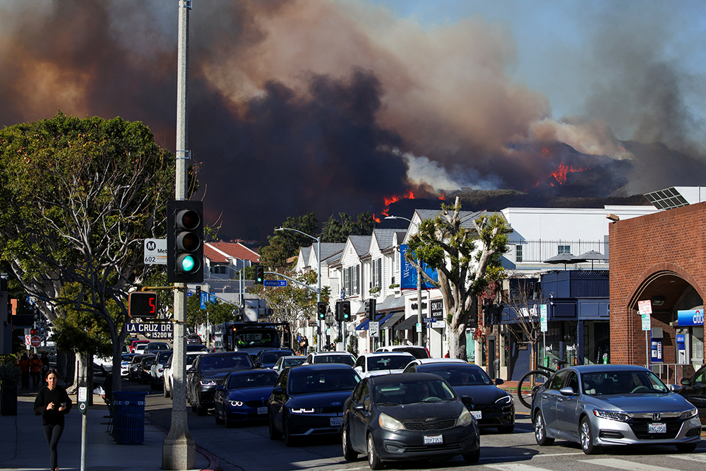 People evacuate as smoke rises from a wildfire burning near Pacific Palisades on the west side of Los Angeles during a weather-driven windstorm in Los Angeles Jan. 7, 2025. Wildfires tore across the Los Angeles area with devastating force Jan. 8 after setting off a desperate escape for residents from burning homes through flames, ferocious winds and towering clouds of smoke. (OSV News/Reuters/Daniel Cole)