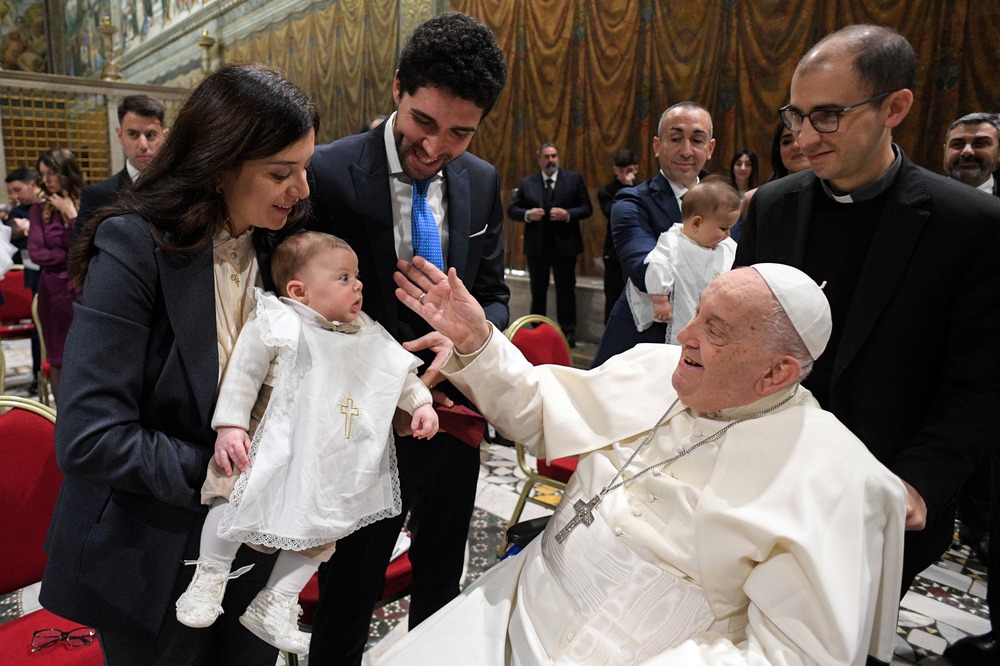 Pope seated in wheelchair, smiles at baby.