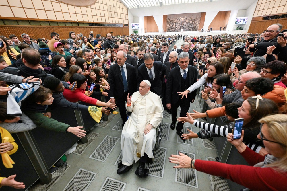 Francis in wheelchair surrounded by people waves and smiles.