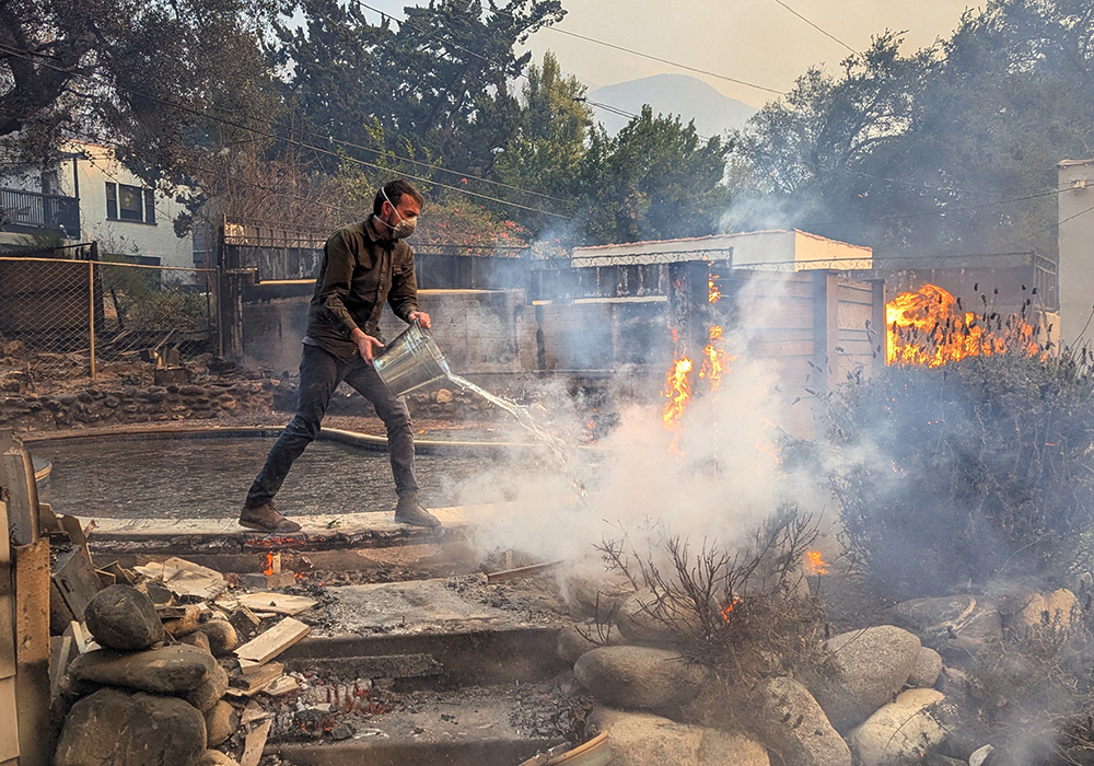 Nick Norman throws a bucket of water on fire in his Altadena neighborhood, Jan. 8 in California. He, wife his Timithie, brother-in-law Mitchell, and others worked to protect their home and others amid ongoing fires in Altadena and the Los Angeles area. (Courtesy of Nick Norman)