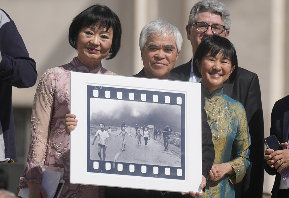 Pulitzer Prize-winning photographer Nick Ut, center, flanked by Kim Phúc, left, holds the "Napalm Girl", his Pulitzer Prize winning photo, as they wait to meet with Pope Francis during the weekly general audience in St. Peter's Square at The Vatican, on May 11, 2022. (AP photo/Gregorio Borgia, file)