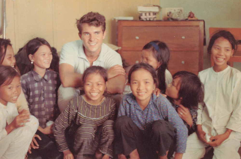 While working for International Voluntary Services in Tuy Hoa, Vietnam, Tom Fox initiated a project where older women taught young girls to make conical straw hats, providing a small source of income. Pictured here is Fox sitting among the hat makers in 1966. (Courtesy of Thomas C. Fox)