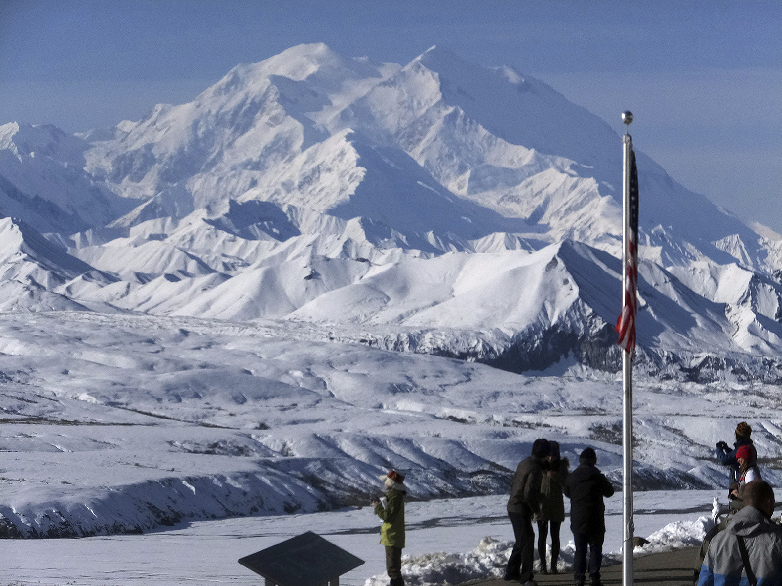 Peak in background, foregrounded are group of people and U.S. flag.