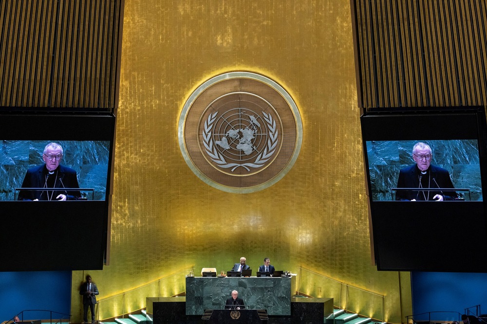 Large United Nations emblem and projector screens showing Parolin speaking.