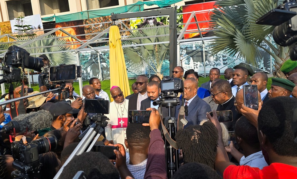 Bishop and priests framed by large swarm of press. 