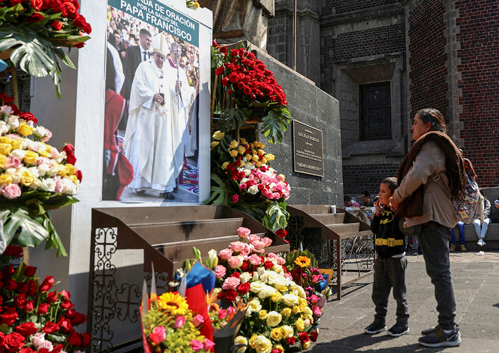 A woman and child stand in front of an image of Pope Francis outside the Basilica of Our Lady of Guadalupe in Mexico City Feb. 23, 2025, after people attended a Mass to pray for the pontiff's health. (OSV News/Reuters/Luis Cortes)