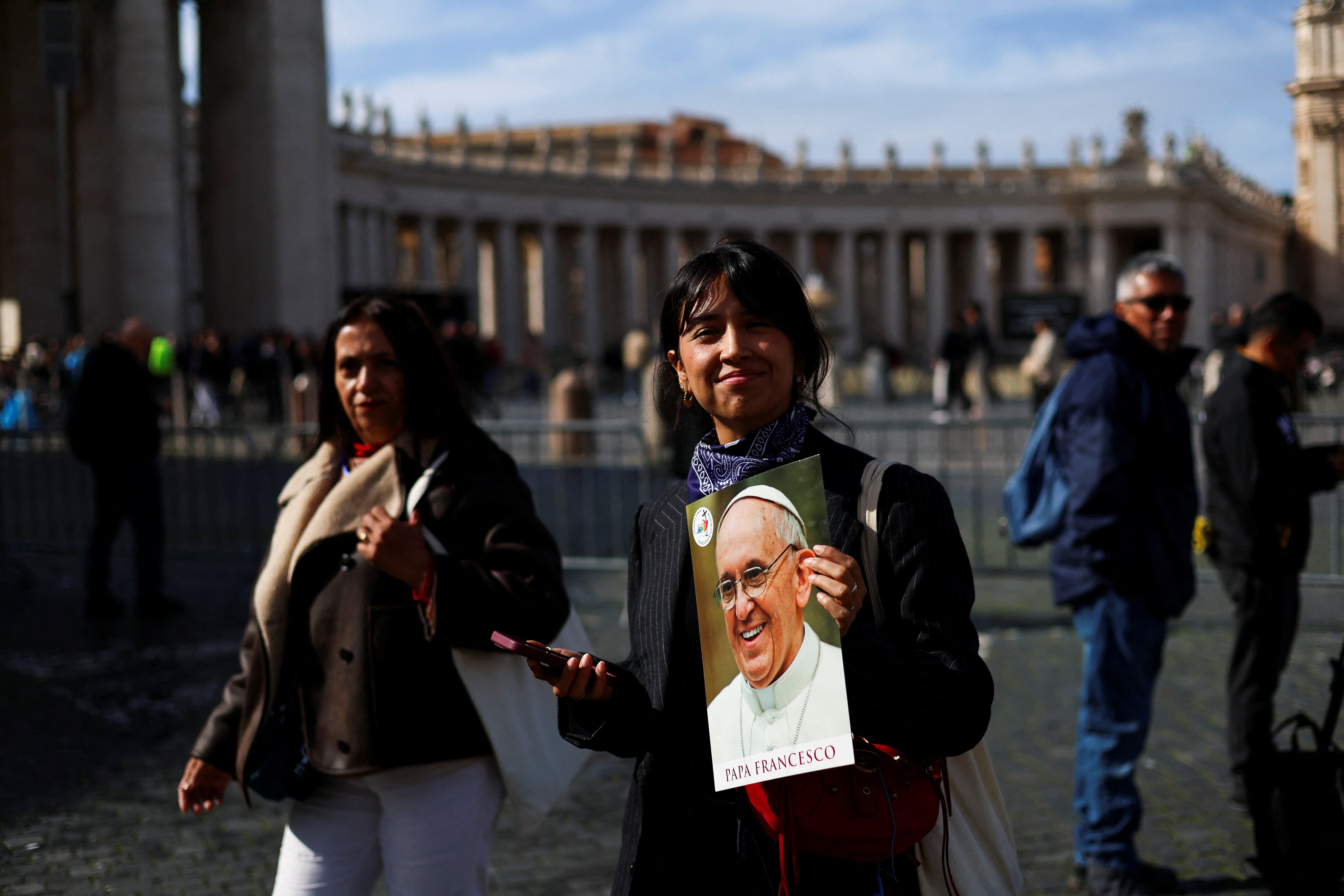  A woman smiles as she holds an image of Pope Francis in St. Peter's Square at the Vatican Feb. 26, 2025, as he continues his treatment for double pneumonia at Rome's Gemelli Hospital. The 88-year-old pontiff had a "restful night" and was sitting upright in an armchair, the Vatican said early Feb. 26. (OSV News photo/Claudia Greco, Reuters)