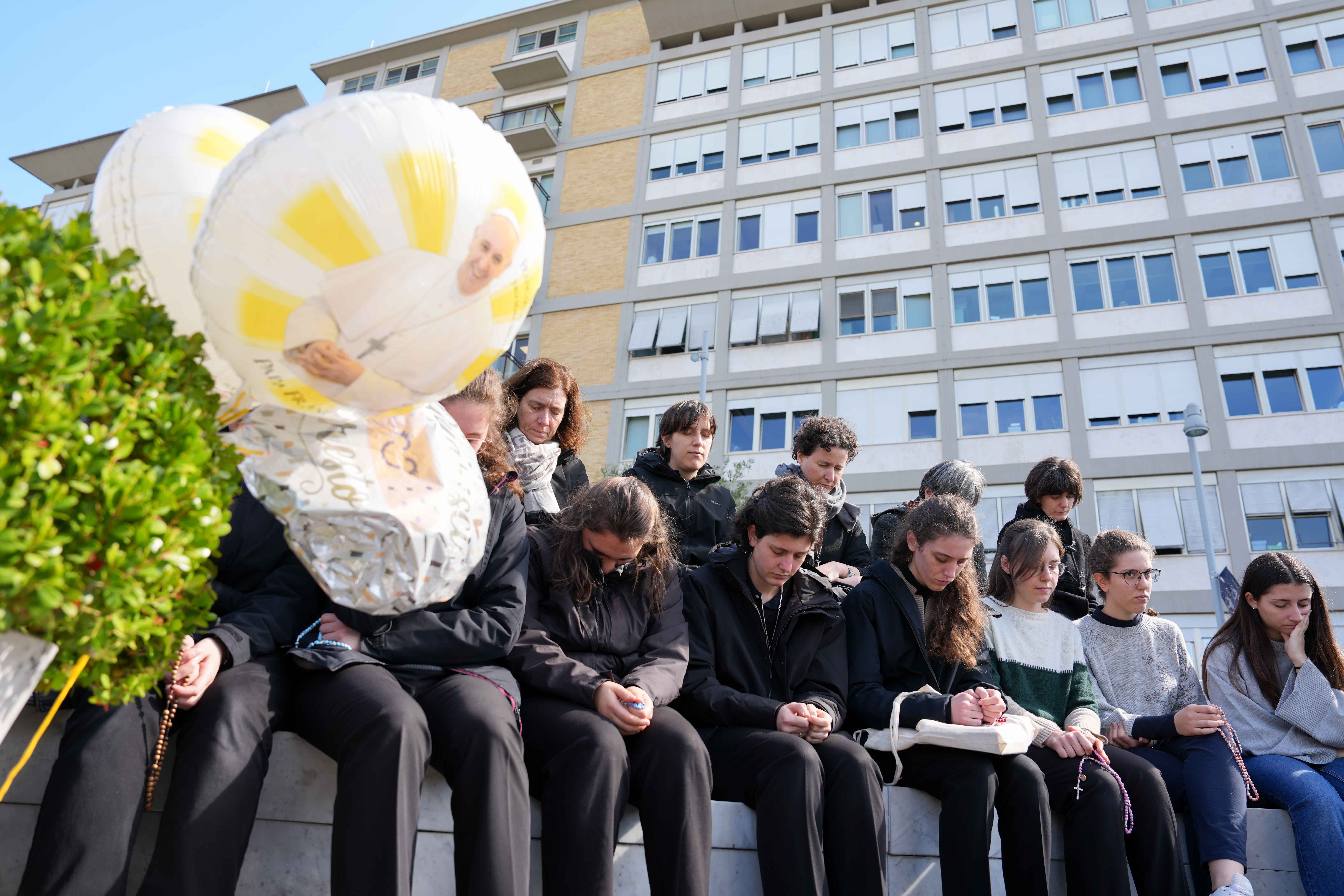 Young people and members of the House of Mary, groups associated with the Pontifical Academy of the Immaculate Conception, pray around a statue of St. John Paul II outside Rome’s Gemelli hospital March 2. Pope Francis is receiving treatment there for double pneumonia. (CNS/Lola Gomez)