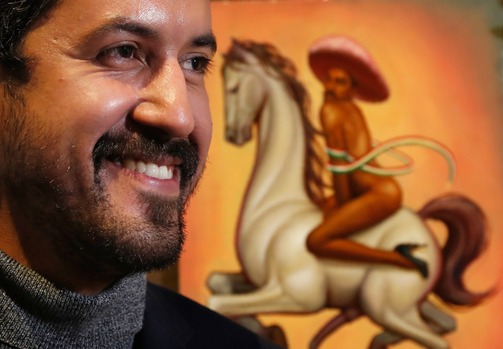 Mexican artist Fabián Cháirez stands next to his painting showing Mexican Revolution hero Emiliano Zapata straddling on a horse nude, wearing high heels and a pink, broad-brimmed, during an interview at the Fine Arts Palace in Mexico City, Wednesday, Dec. 11, 2019.