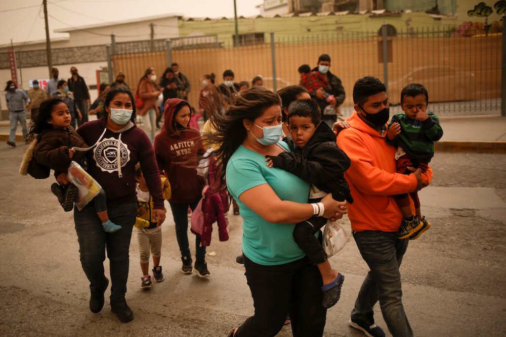 People from Central America wearing masks and carrying children outside near the Paso del Norte international border bridge in Ciudad Juárez, Mexico