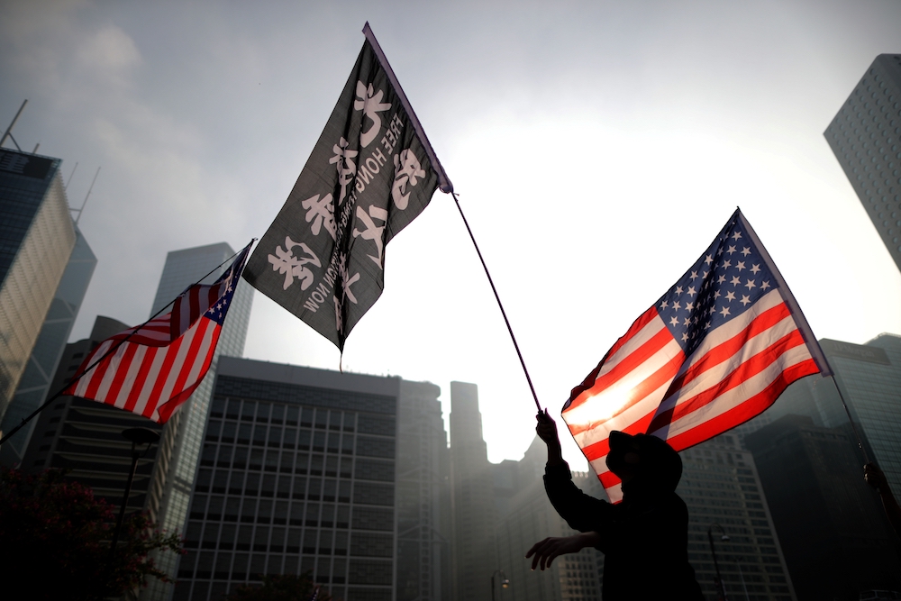 people waving US flags and a flag with Chinese writing seen against buildings