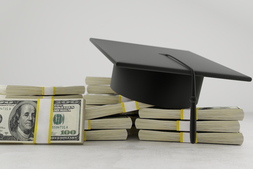 A college mortarboard hat resting on bundles of 100 dollar bills