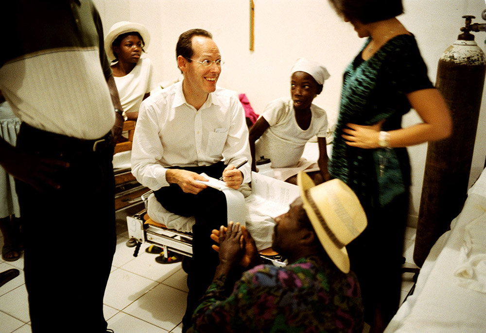 Dr. Paul Farmer sits with a young leukemia patient, Marta Cassmand, in Cange, Haiti, in January 2004. Marta's father, Sanoit Valceus (foreground), had cut a tendon in his hand and was asking Farmer for advice. (Newscom/PSG/St. Petersburg Times)