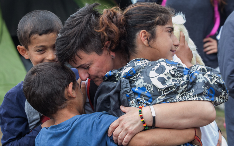 A volunteer from a humanitarian organization hugs refugee children June 13 during a police operation at a makeshift camp in Polykastro, Greece. (CNS/Nikos Arvantidis, pool via EPA)