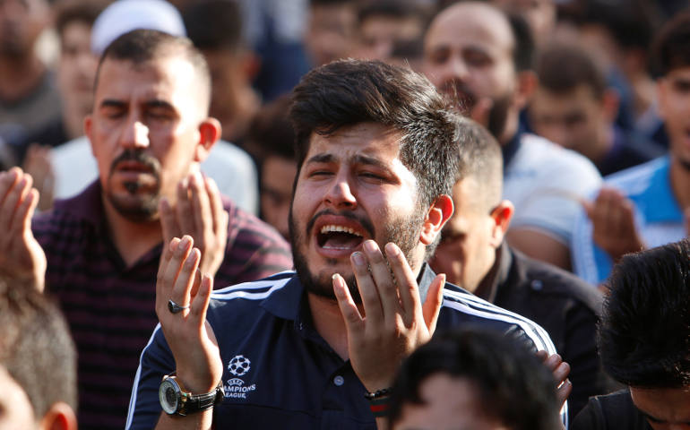 Muslim men pray July 6 at the site of a July 3 suicide car bomb attack at a shopping area in Baghdad. (CNS photo/Khalid-Mousily, Reuters)