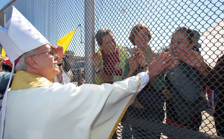 Bishop Mark Seitz of El Paso, Texas, touches the hands of people in Mexico through a border fence following Mass in Sunland Park, N.M., in this 2014 file photo. (CNS/Bob Roller)