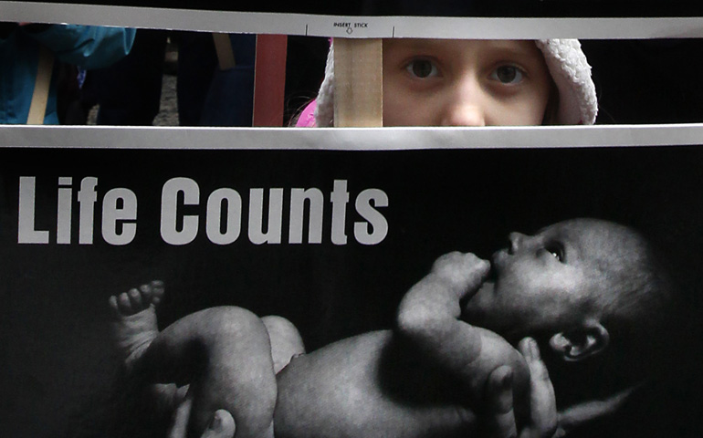 A girl peeks through signs as she walks through downtown Chicago during the city's Jan. 18 March for Life. (CNS/Catholic New World/Karen Callaway)