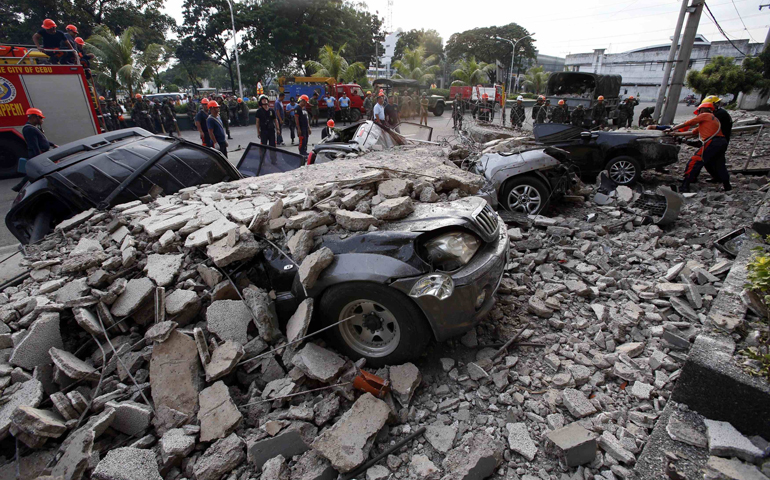 Firefighters stand near destroyed vehicles covered with rubble after an earthquake struck Cebu City, Philippines, on Tuesday. (CNS/Reuters/ Erik De Castro)