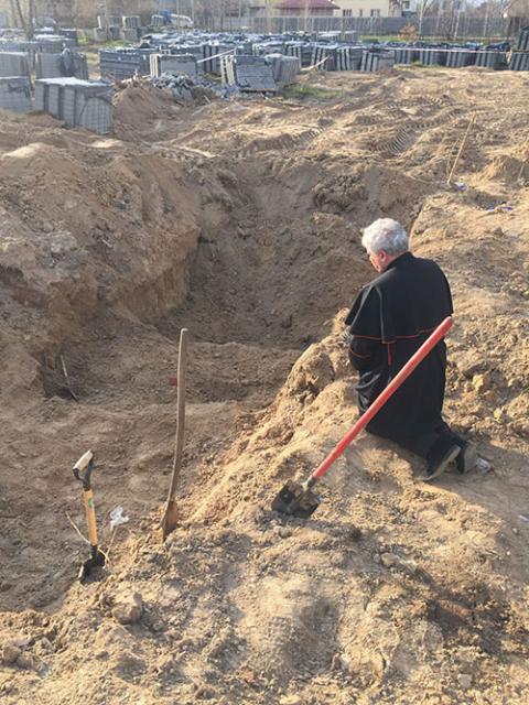 Cardinal Konrad Krajewski prays over a mass grave near Borodyanka, Ukraine, April 15, during a humanitarian visit as a papal envoy to the country. (CNS/Vatican Media)