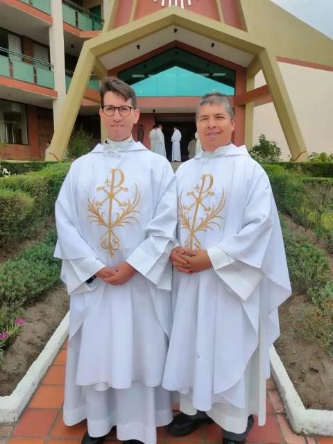 Arcos poses for picture next to other pries; both wear white chasubles.