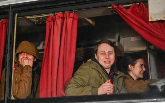 Ukrainian women wearing green coats stare emotionally out of windows on a bus or train