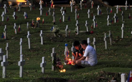 Filipinos light candles in front of the tomb of their deceased loved one, inside a military cemetery near Manila, Philippines, Oct. 31, 2015. Filipinos flock to cemeteries across the country to commemorate their departed loved ones for All Saints' Day and All Souls' Day. (CNS photo/Romeo Ranoco, Reuters)