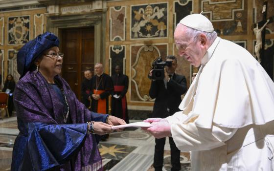 An elegantly dressed Black woman hands Pope Francis a letter