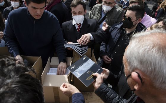 A book commemorating Pope Francis' March 27, 2020, prayer service at the beginning of the COVID-19 pandemic is distributed to people in St. Peter's Square after the pope's Sunday Angelus at the Vatican March 27, 2022. (CNS photo/Vatican Media)