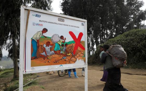 Women in Rubaya, Congo, walk past a sign warning against child labor.