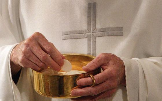 A priest holds bowl with Communion wafers.