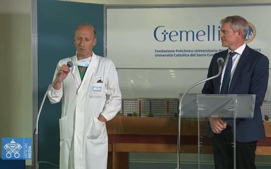 Matteo Bruni, director of the Vatican Press Office, looks at Dr. Sergio Alfieri, a chief surgeon at Rome's Gemelli's hospital, who operated on Pope Francis June 7, 2023, and speaks to reporters at the hospital as seen in this screengrab of the news conference broadcast live by Vatican Media. Alfieri said the pope was recoverying well from a three-hour surgery for a hernia. (CNS screengrab/Courtesy Vatican Media)