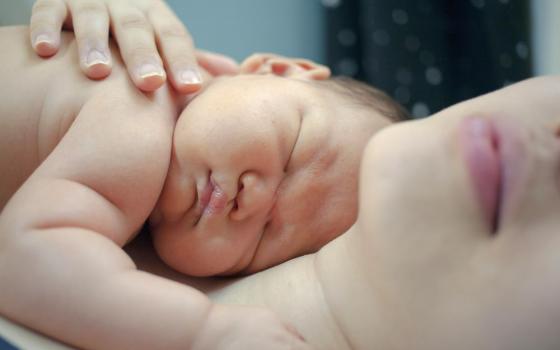 Woman hugs baby on her chest.