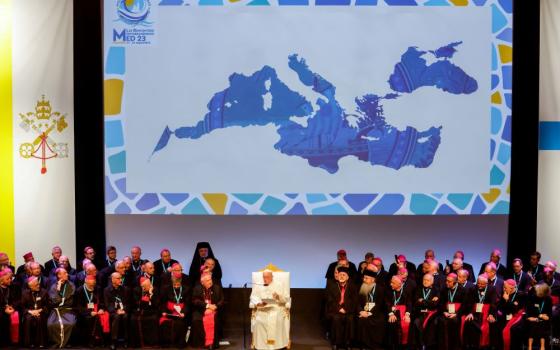 Pope sits with bishops in front of a large map of the Mediterranean region.