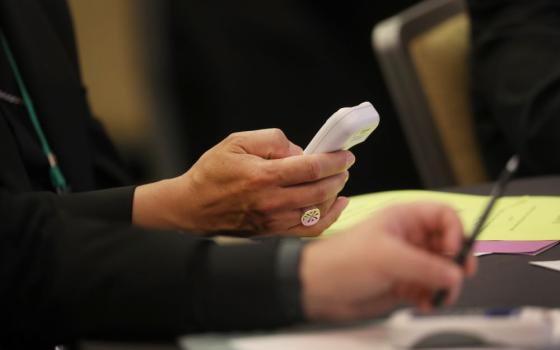 A bishop hands are shown, holding a cellphone size device to cast votes. 