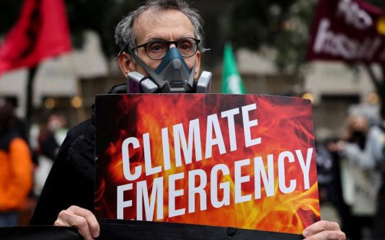 Man with mask holds sign that reads, "Climate Emergency."