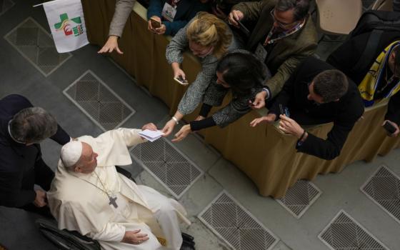 An overhead view of Pope Francis sitting in a wheelchair and shaking the hands of onlookers