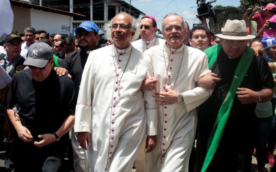 Three men in white cassocks stand among laymen and priests. Two of the men in white cassocks link arms.