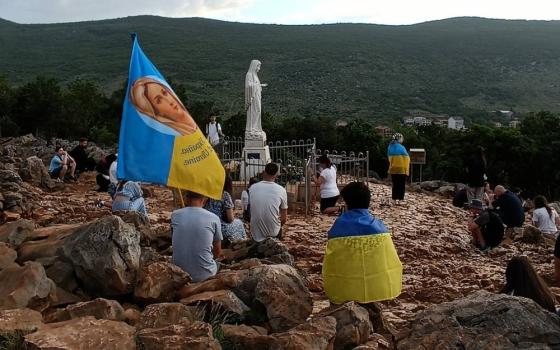 Children sit on rocky mound, draped in Ukrainian flags.