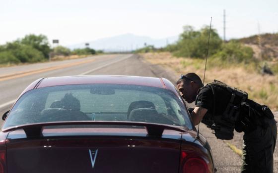 Officer leans into passenger window of red car on long desert road