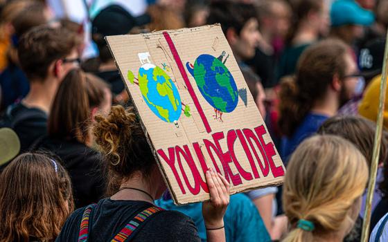 Protester holds a sign with painted images of two Earths and the words "YOU DECIDE" (Pixabay/dmncwndrich)