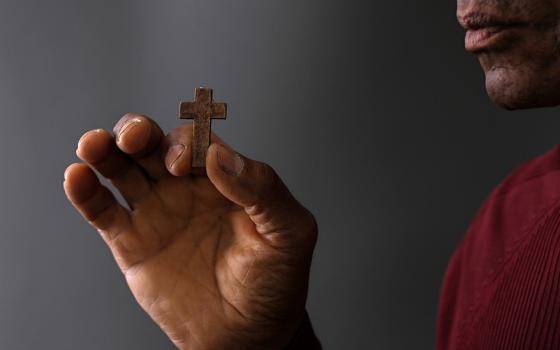 A black man holds in front of him a small wooden cross (Dreamstime/Derektenhue)