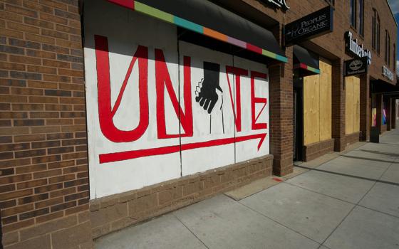 A white sign with clasped hands and the word UNITE in red on the side of a building (Unsplash/Priscilla Gyamfi)