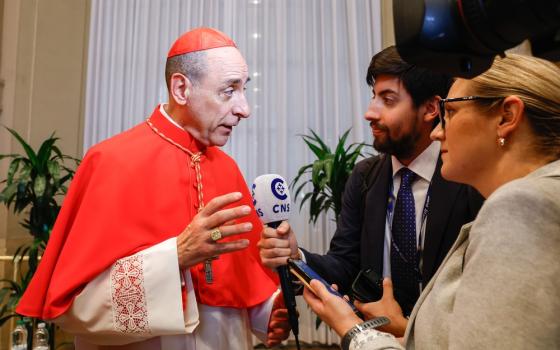 Fernandez wears red Cardinal's clerics and speaks to reporters. 